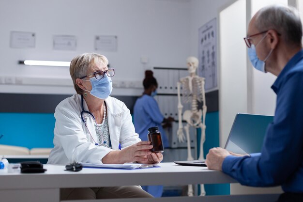 Huisarts die fles pillen geeft aan bejaarde man om ziekte te genezen bij controlebezoek, tijdens pandemie. Specialist die een pot met voorgeschreven medicijnen vasthoudt aan een zieke patiënt met een gezichtsmasker.