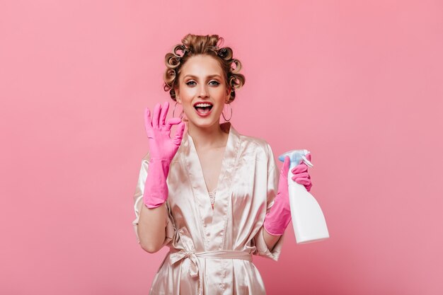 Huisvrouw in roze handschoenen houdt glazenwasser en toont ok teken