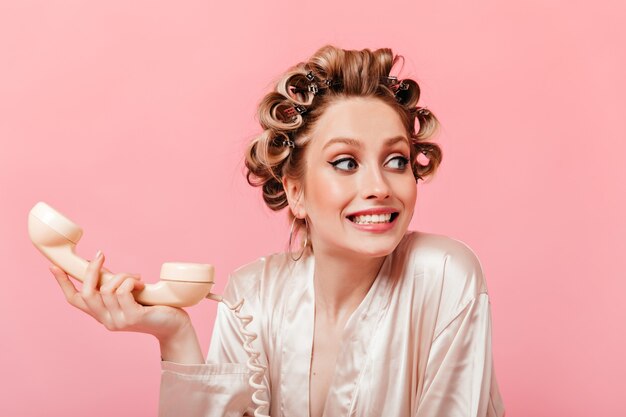 Huisvrouw in zijden blouse voelt zich ongemakkelijk en houdt vaste telefoon vast aan de roze muur