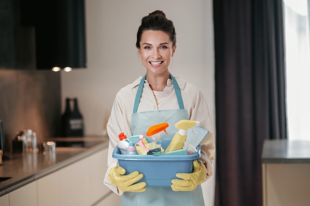 Gratis foto huisvrouw. jonge lachende vrouw met een bassin met reinigingsapparatuur