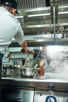 Hulp in de keuken. verticale foto van een jonge professionele chef-kok die een pepermolen aan zijn assistent geeft tijdens het kookproces.