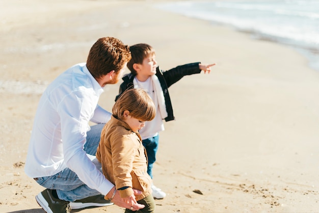 Hurkende vader met zonen op het strand