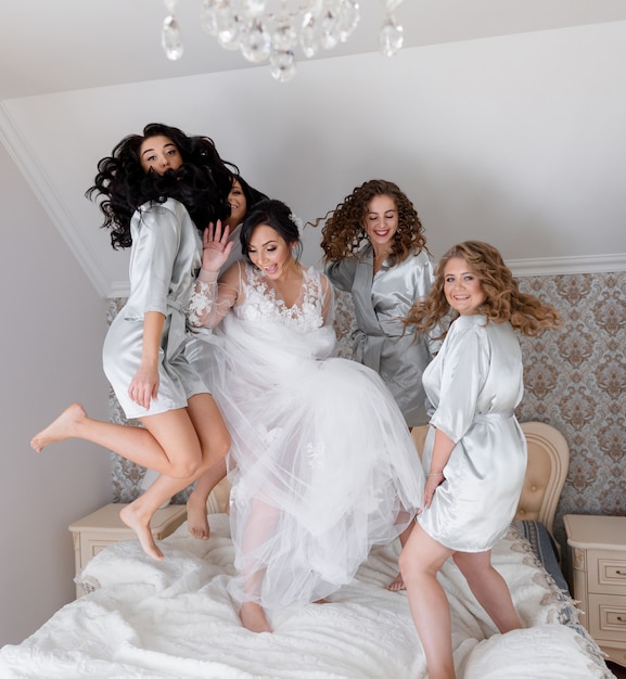 Gratis foto huwelijksochtend springt de bruid met bruidsmeisjes vrolijk op het bed en lacht