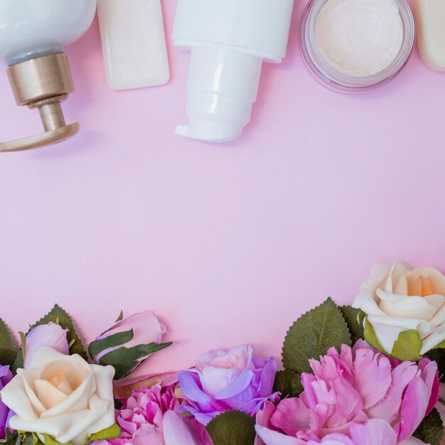 Hydraterende crème en nep bloemen op roze oppervlak