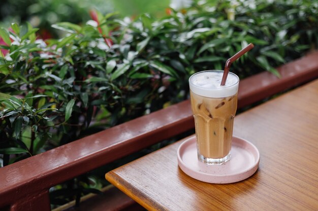 Iced latte in glas op een roze stand op houten tafel in zomerterras groene struiken