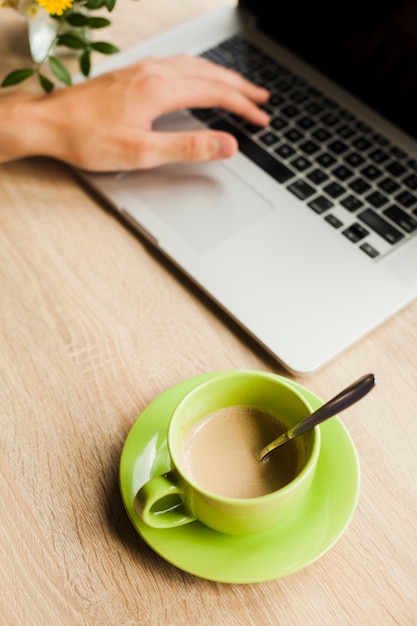 Iemands hand met laptop met een kopje koffie op houten bureau