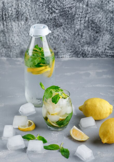 IJzig detox water met citroenen, mint in glas en fles op grijze en grungy oppervlak