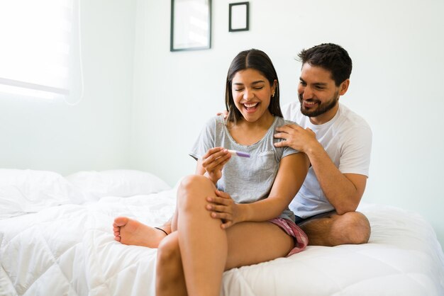 Ik ben zwanger! Goregous gelukkige vrouw van in de twintig voelt zich opgewonden vanwege haar positieve zwangerschapstest en viert feest met haar vriendje