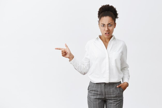 Ik ga niet in die auto zitten. Ontevreden ondervraagde Afro-Amerikaanse vrouwelijke zakenpartner in glazen en wit overhemd, hand in hand in broek, naar links wijzend en starend met afkeer en twijfel