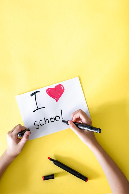 Gratis foto ik hou van school, de hand van het kind schrijft in een papier op een gele achtergrond