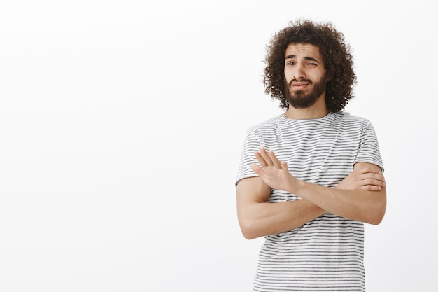 Ik koop dat niet. Portret van niet onder de indruk van aantrekkelijke Oost-man met krullend haar en baard in gestreept shirt, handen kruisen en palm tonen in nee of stop gebaar