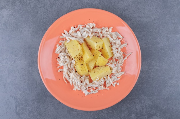 In blokjes gesneden kip met gekookte aardappelen op oranje plaat.