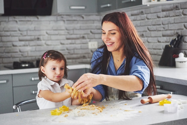 In de keuken en gelukkige familie. De moeder en de dochter die het deeg voorbereiden, bakken koekjes.