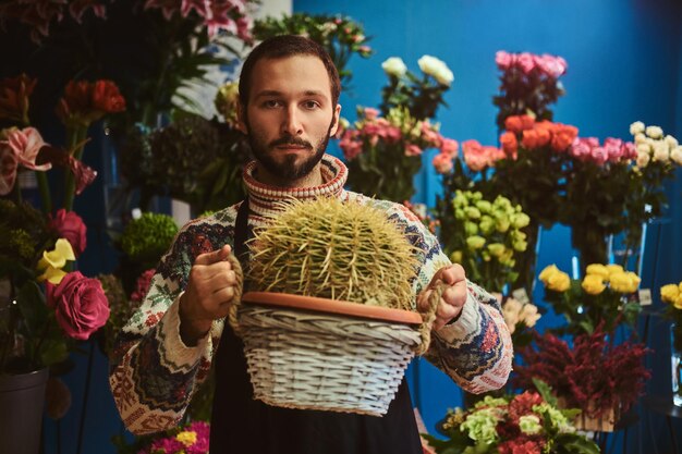 In een mooie bloemenwinkel geeft de jonge arbeider grote cactus in een mand.