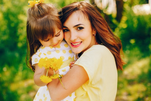in een zomerpark bij groene bomen loopt mama in een gele jurk en haar kleine mooie meisje