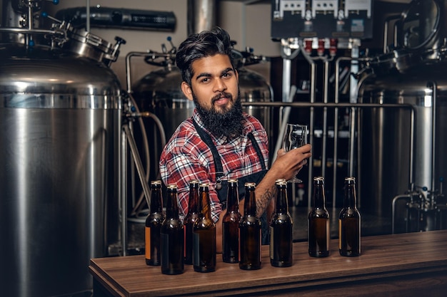 Indiase bebaarde getatoeëerde hipster mannelijke fabrikant die ambachtelijk bier presenteert in de microbrouwerij.