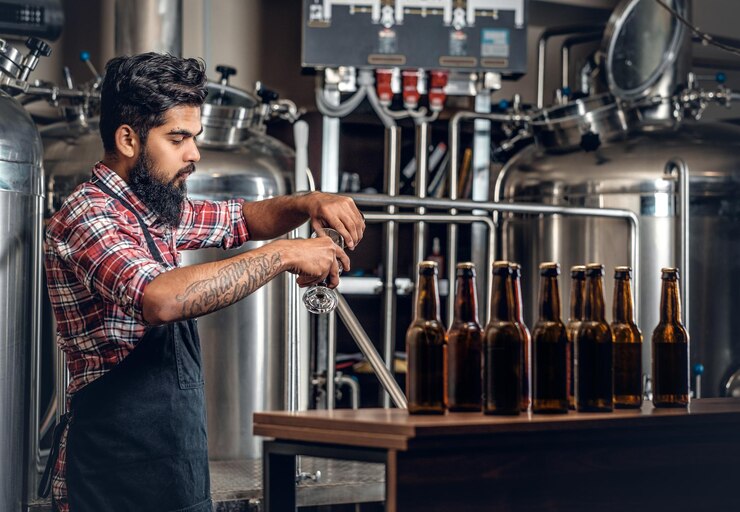Gratis Foto indiase bebaarde getatoeëerde hipster mannelijke fabrikant die ambachtelijk bier presenteert in de microbrouwerij.