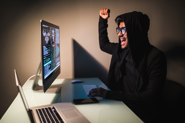 Indiase hacker draagt een masker met behulp van een laptop in de lege witte kamer.