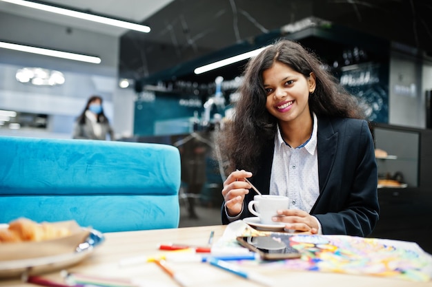 Indiase kunstenaarsvrouw draagt een formele verffoto en drinkt thee terwijl ze in café zit