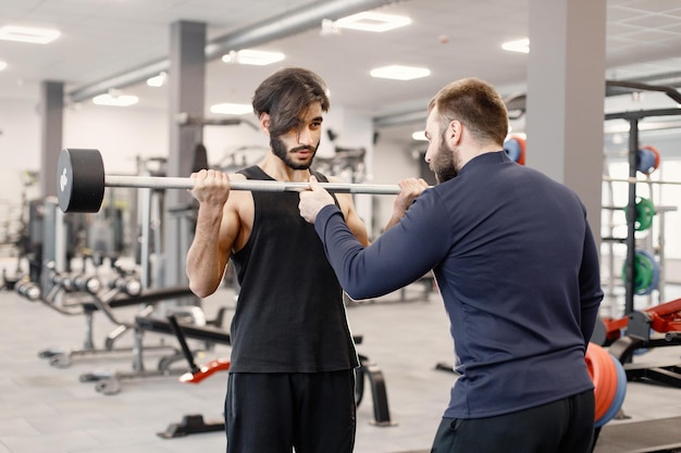 Indiase man doet oefeningen op speciale apparatuur in de sportschool met personal trainer