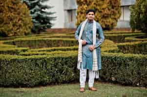 Gratis foto indiase man draagt traditionele kleding met witte sjaal buiten tegen groene struiken in het park