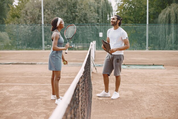 Indiase man en zwarte Amerikaanse vrouw staan op een tennisbaan