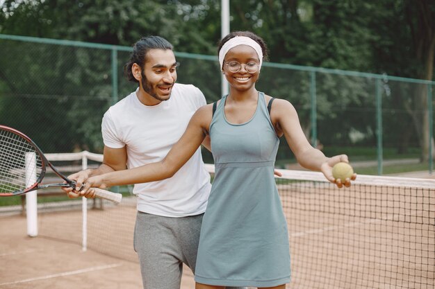 Indiase man en zwarte Amerikaanse vrouw staan op een tennisbaan