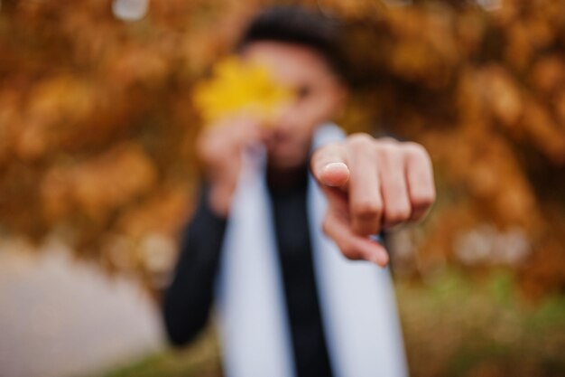 Indiase stijlvolle man in zwarte traditionele kleding met witte sjaal buiten geposeerd tegen gele herfst en vinger laten zien