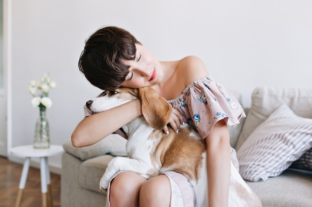 Indoor portret van dromerige bruinharige meisje in vintage kleding beagle hond met gesloten ogen omarmen