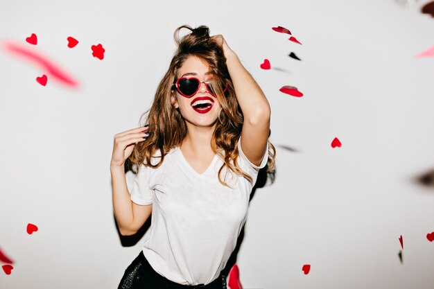 Indoor portret van geweldig vrouwelijk model in trendy t-shirt aan haar lange glanzende haren te raken