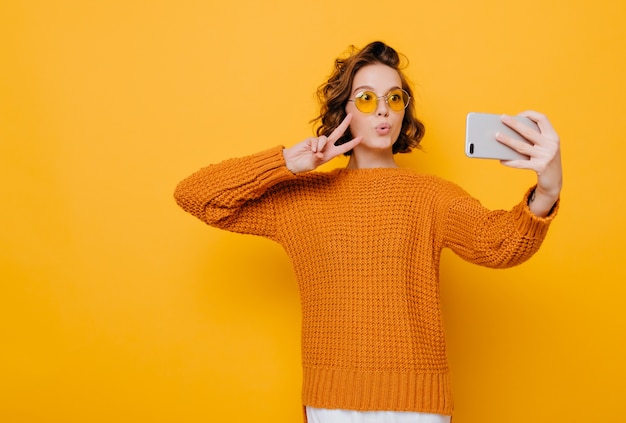 Indoor portret van leuke vrouw in zachte gebreide kleding poseren met vredesteken