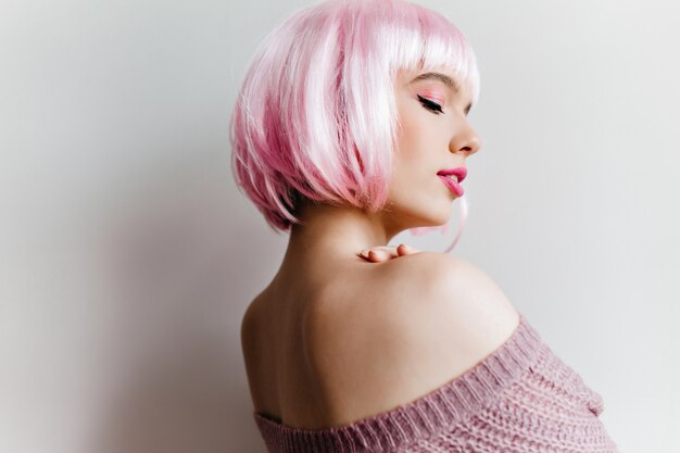 Indoor portret van sierlijke witte vrouw poseren met plezier Foto van mooi meisje in roze peruke dromen over iets.