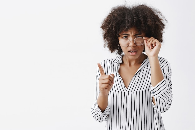 Gratis foto indoor shot van intens verward en ontevreden vrouwelijke donkerhuidige lerares met een afrokapsel die van onder een bril kijkt die de rand aanraakt en de wijsvinger schudt in een uitbrander gebaar wordt afgekeurd