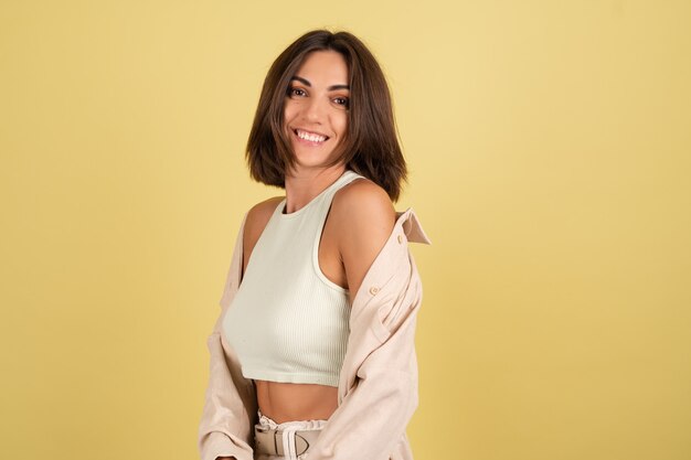 Indoor studio portret van gelukkige vrouw met witte top en open t-shirt op geel