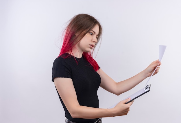 Indrukwekkende jonge mooie vrouw die een zwart t-shirt draagt dat door klembord in haar hand op geïsoleerde witte muur bladert