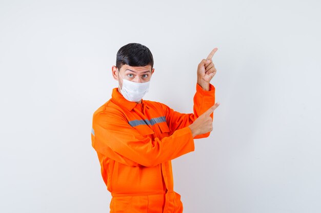 Industriële man in uniform, masker wijzend naar de rechterbovenhoek, vooraanzicht.