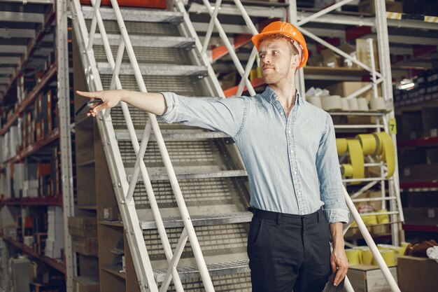 Industriële werknemer binnenshuis in fabriek. Zakenman met oranje bouwvakker. Man in een blauw shirt.