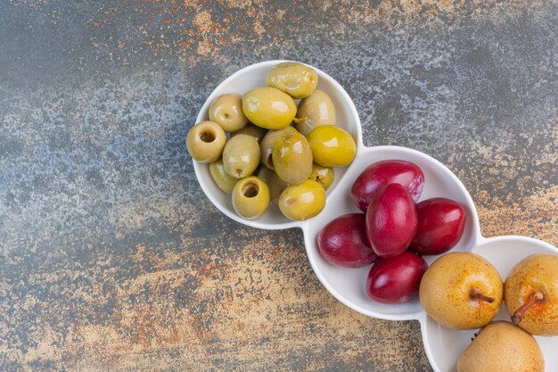 Ingeblikte appel, pruimen en olijven op een schotel