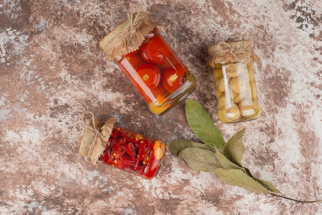 Ingemaakte rode paprika, tomaten en champignons in een glazen pot op marmeren tafel.