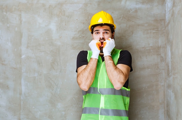 Gratis foto ingenieur in gele helm en industriële handschoenen ziet er bang en doodsbang uit