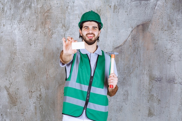 Ingenieur in gele uitrusting en helm die een houten behandelde bijl houdt en zijn visitekaartje voorstelt.