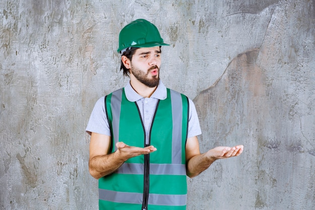 Ingenieur in gele uitrusting en helm die op betonnen muur staat en interactie heeft met de persoon die voor je ligt.