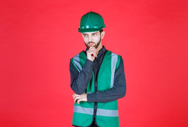 Ingenieur in groen uniform en helm denken en plannen.