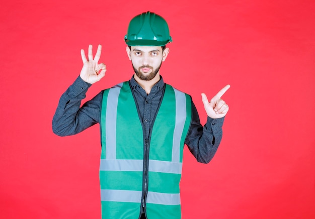 Gratis foto ingenieur in groen uniform en helm die plezierteken tonen.