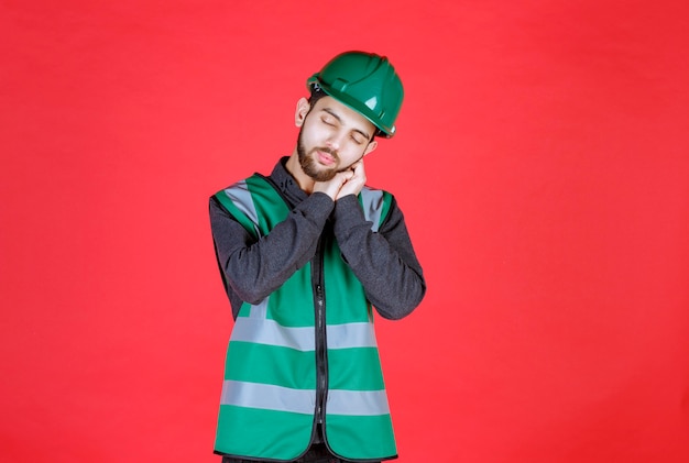 Ingenieur in groen uniform en helm ziet er moe en slaperig uit.