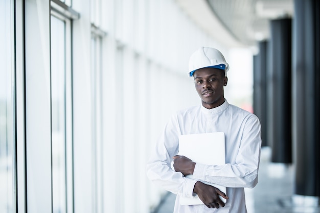 Gratis foto ingenieur in veiligheidshelm die zich met laptop computer in bureau dichtbij panoramisch venster bevindt