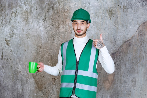 Ingenieur man in geel uniform en helm met een groene koffiemok en genietend van het product.