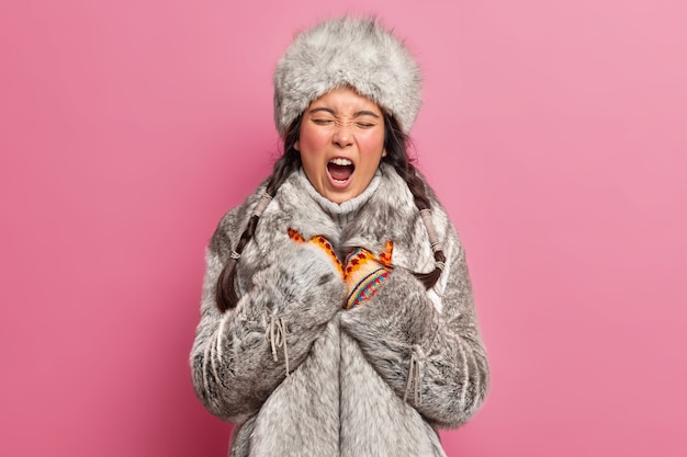 Inheemse vrouw gaapt en heeft een slaperige uitdrukking op winterkleren, leeft op groenland poseert tegen een roze muur