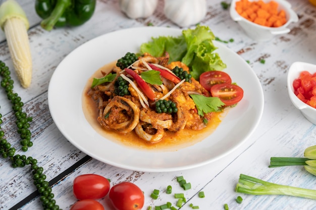 Inktvis gebakken met currypasta in witte plaat, met groenten en bijgerechten op een witte houten vloer.