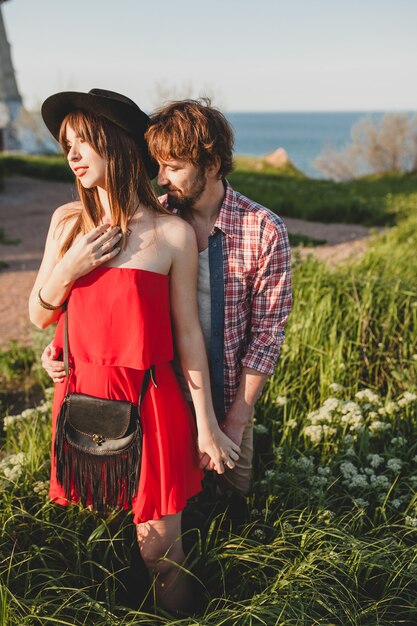 Inschrijving jonge stijlvolle paar verliefd op platteland, indie hipster bohemien stijl, weekendvakantie, zomer outfit, rode jurk, groen gras, hand in hand, glimlachen